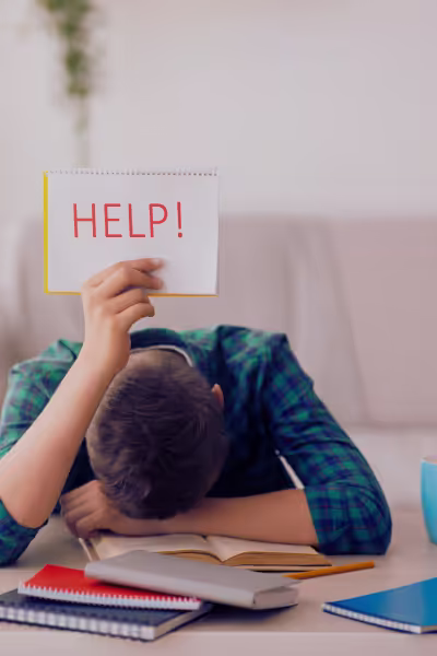 A man sitting at a desk, facedown, holding up a sign saying "HELP"