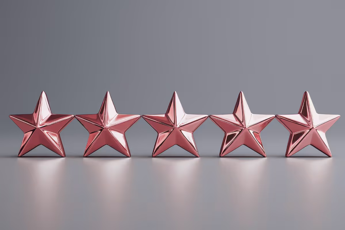 The image shows a grey background. Roughly two thirds of the background is matt grey. The bottom third is a glossy grey surface. There are 5 metallic bronze stars in the middle third and their reflection is showing on the glossy surface.